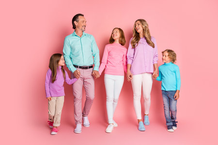 Happy family in pastel outfits holding hands against pink background showing love together and joy in a warm family momentの写真素材