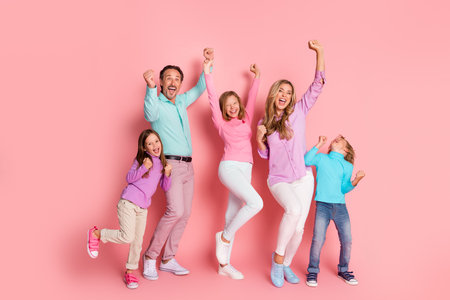Family celebration of love and togetherness as parents and children cheer jump and pose against a pink background in a bright joyful day of fun and holiday spiritの写真素材