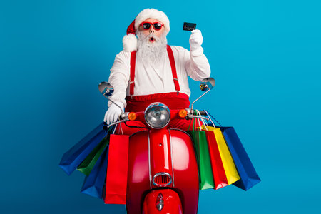 Santa on a bright red scooter surrounded by colorful shopping bags delivering festive holiday vibes and Christmas joy in a fun stylish season shopping sceneの写真素材