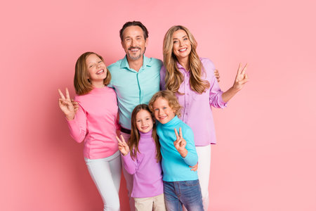 Happy family portrait with parents and three kids smiling together against a pink background for...