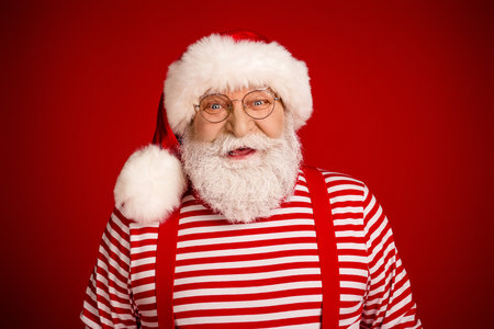 Santa with striped shirt red suspenders and hat smiles warmly against a festive red background ready for Christmas adsの写真素材