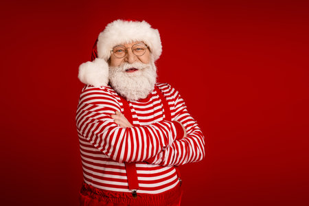 Santa with striped shirt and red suspenders stands against bold red background delivering a festive portrait that captures Christmas joy and holiday cheerの写真素材