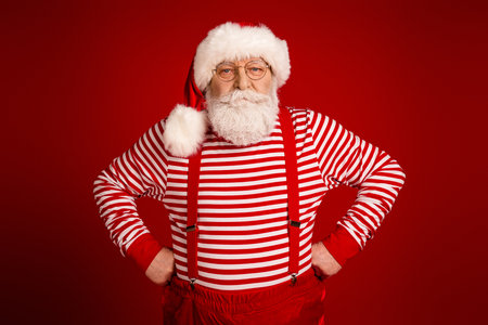 Santa in striped shirt with red suspenders posing in bright red studio for Christmas promotion and holiday family contentの写真素材