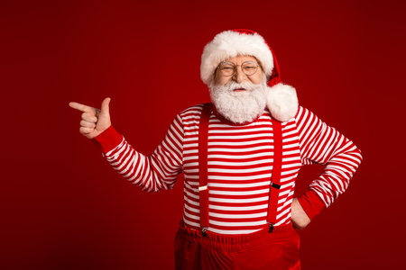 Santa Claus in striped red and white outfit with suspenders points confidently in a festive holiday scene for Christmas advertisingの写真素材