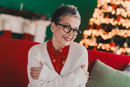 Charming senior woman celebrating festive holiday season in cozy indoor setting with Christmas decorations and warm atmosphereの写真素材