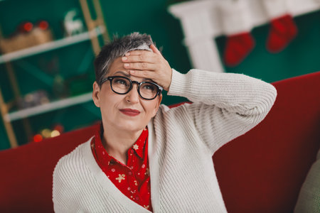 Elderly woman in festive cardigan indoors against Christmas decorations and atmosphere, embracing the holiday spiritの写真素材