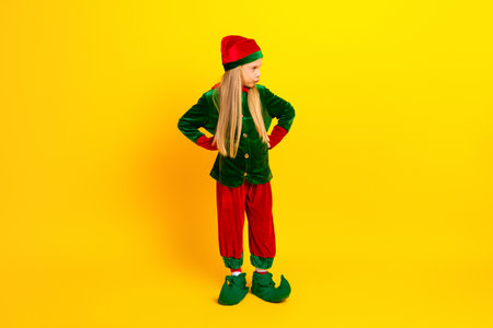 Young girl dressed as a festive elf in a bright holiday costume posing against vibrant yellow backdrop celebrating Christmasの写真素材