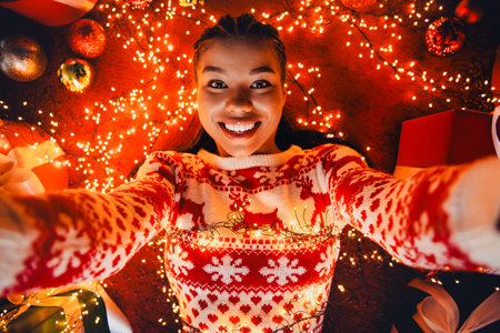 Funny cozy christmas moment a joyful woman in a festive sweater holds lights for a playful home celebrationの写真素材