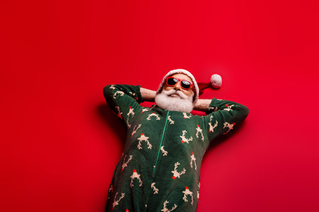Santa in festive pajama relaxes in a bold red setting with a playful vibe perfect for holiday cheerの写真素材