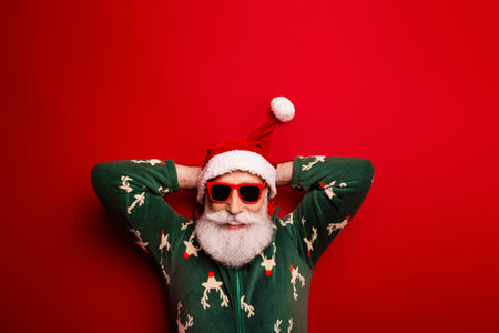 Santa in a festive red scene wearing a green reindeer sweater and sunglasses lounges with hands behind head for a playful holiday portraitの写真素材