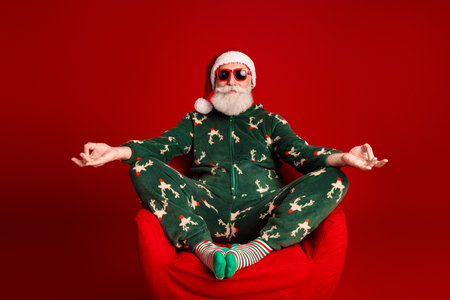 Santa in christmas pajamas relaxes in a red chair for a fun festive stock photoの写真素材