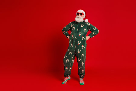 Santa in green Christmas pajama with reindeer print poses on red background for stock listing bright funny festive season style and holiday cheerの写真素材