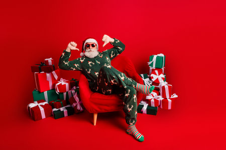 Santa relaxes in a cozy red room surrounded by gifts wearing a festive pajama suit and striped socks for a cheerful holiday sceneの写真素材