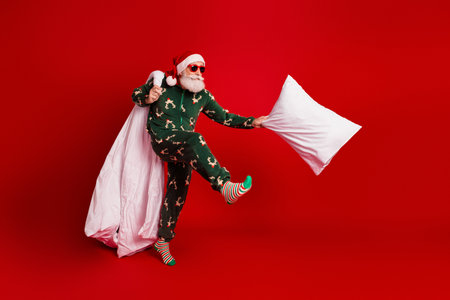 Santa in green pajama with red background engages pillow fight creating merry holiday energy for christmas themed campaignの写真素材