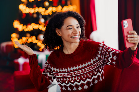 Playful holiday selfie moment with a smiling woman in a red sweater by a lit Christmas treeの写真素材