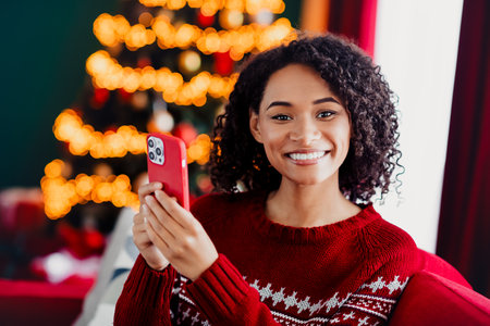 Playful Christmas selfie by the twinkling tree as she chats on her phone sharing warm holiday joyの写真素材