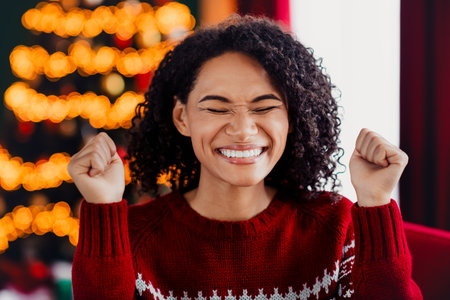 Hilarious festive moment smiling woman in red sweater celebrating Christmas at home with warm lights and tree joy around usの写真素材