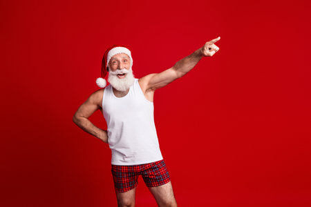 Santa in casual sleepwear strikes a playful pose against a bright red backgroundの写真素材