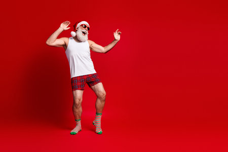 Festive santa in casual sleepwear dances in front of red background for holiday cheerの写真素材