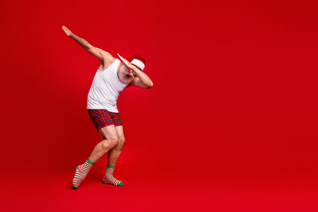 Festive Santa look man in pajama shorts dancing against a bold red background perfect for Christmas and holiday themed campaignsの写真素材