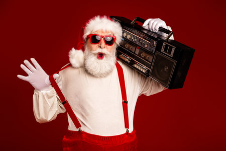 Santa Claus with red suspenders and white beard carries a retro boombox in a festive Christmas scene ready to spread music and joyの写真素材