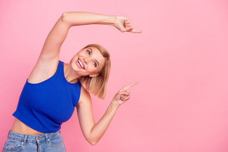 Portrait of nice young girl indicate fingers empty space wear blue top isolated on pink color backgroundの写真素材