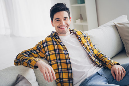 Photo of cheerful positive guy dressed plaid shirt relaxing sofa enjoying weekend indoors room home houseの写真素材