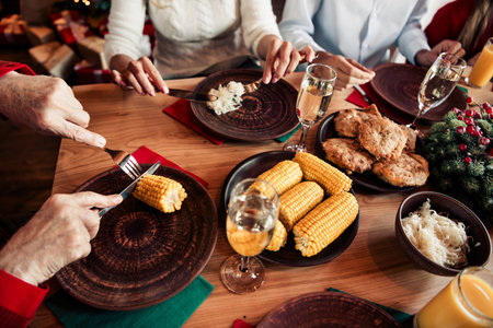 Festive family dinner around a wooden table with corn on the cob fried chicken and drinks as Christmas decorations glowの写真素材