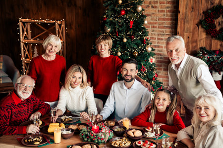 A joyful family Christmas dinner around a festively decorated table with a large tree and warming indoor decor for a cozy holiday celebrationの写真素材