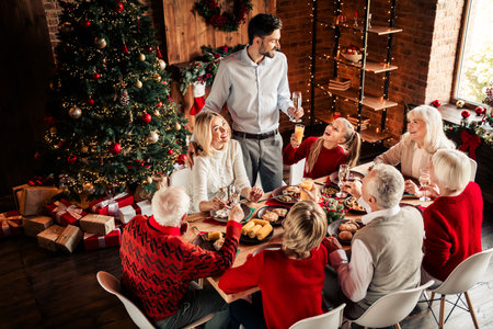 Family gathers for a Christmas dinner around a festive table in a warm home beside a twinkling Christmas tree for a cozy celebration of togetherness and holiday joyの写真素材
