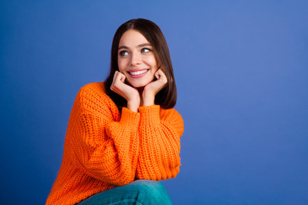 Portrait of a young woman in an orange sweater smiling against a blue backgroundの写真素材
