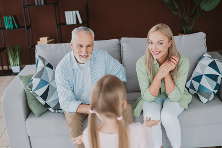 fun family moment with mom dad and daughter relaxing together on the sofa at home sharing smiles and warm comfortの写真素材
