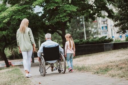 Funny gentle stroll in park with grandpa in wheelchair and family by his side sharing love and support and laughterの写真素材