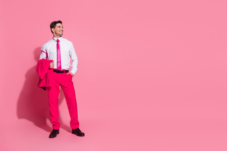 Confident young man in vibrant pink suit posing against pink background showcasing elegance, fashion, and a modern stylish vibeの写真素材