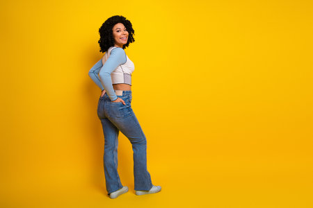 Beautiful young woman smiling against a vibrant yellow background wearing a casual outfit and jeans