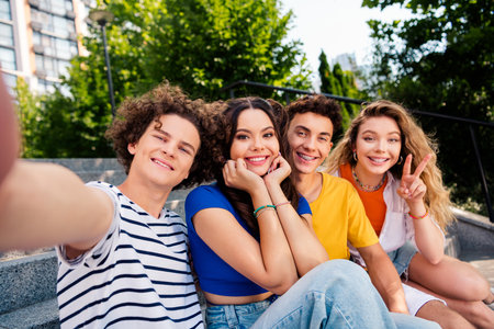 Group of cheerful young friends taking a selfie outdoors, enjoying a sunny day, embracing camaraderie and happiness togetherの写真素材