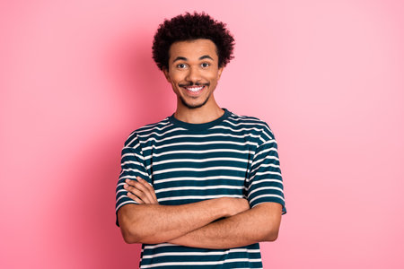Young mixed race male model with shirt stands against a pink background smiling confidently...