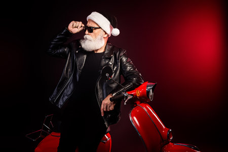 Santa rocker on a red scooter in a leather jacket with sunglass and beard exuding modern christmas vibeの写真素材