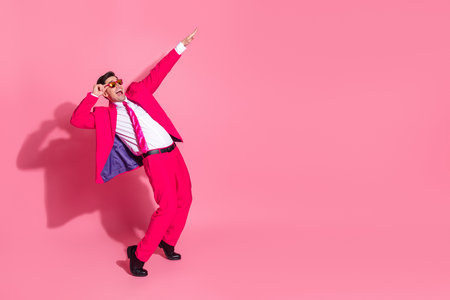 Young man in a vibrant pink suit posing stylishly on a bright pink background, showcasing charisma and modern attitudeの写真素材