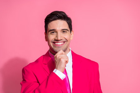 Stylish young man in vibrant pink suit posing against pink background smiling confidently with a charming expressionの写真素材