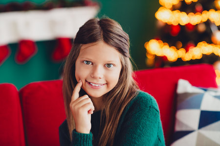 funny cozy christmas moment a smiling girl on a red sofa by the tree at home during winter...