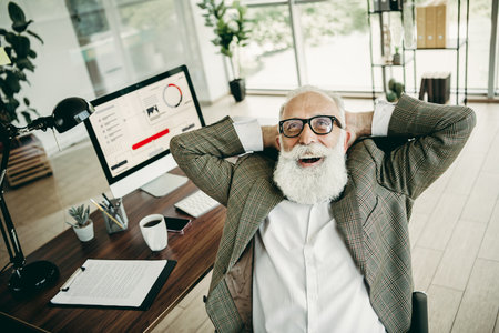 Elderly businessman relaxing in an office chair expressing confidence and satisfaction at his workspaceの写真素材