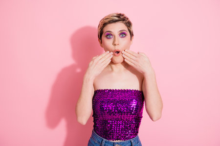 Young glamour woman with pink backdrop wearing sequins top expresses surprise in a playful fashion...