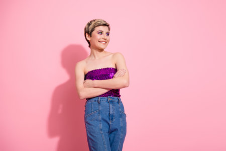 Young woman with short blond hair wearing pink sequins top and jeans smiles confidently against pink...