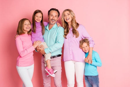 Happy pastel family portrait with parents and kids smiling together in a pink studio background for holiday marketingの写真素材