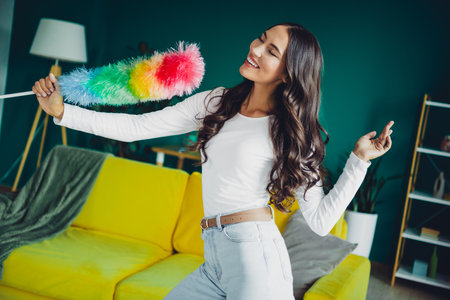 Joyful woman dances with rainbow duster at home in colorful living roomの写真素材