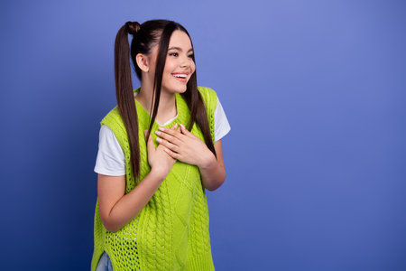 Happy young woman in a neon green vest smiles with hands on her chest against a blue backdropの写真素材