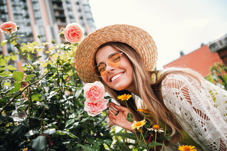 Happy traveler woman in sunhat posing among roses during a sunny city garden strollの写真素材