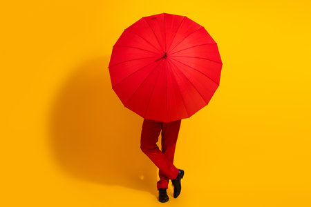 Playful red umbrella surprise in a bright yellow studio setting with a stylish man in a red suit striking a chic poseの写真素材