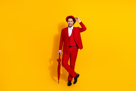 Playful red suit showman strikes a stylish pose with umbrella against bold yellow background for a fun fashion promoの写真素材